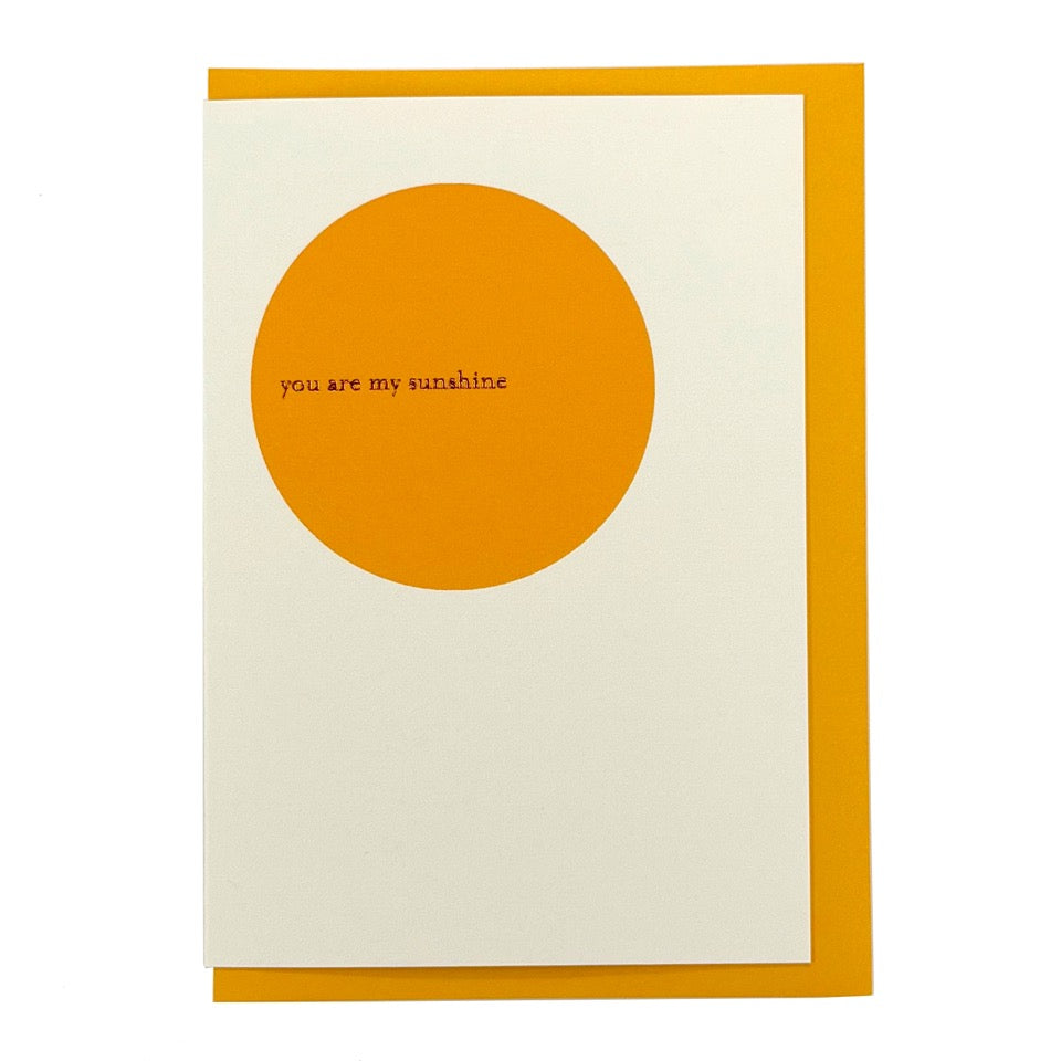 Minimalist greeting card featuring a bold golden yellow circle with the words "you are my sunshine" in delicate gold foil, paired with a mustard yellow envelope.
