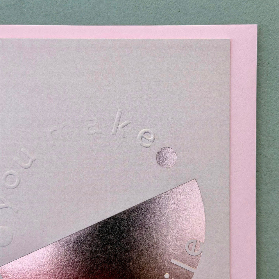 Close-up of the embossed lettering and pink foil detail on the pale lilac You Make Me Smile card.
