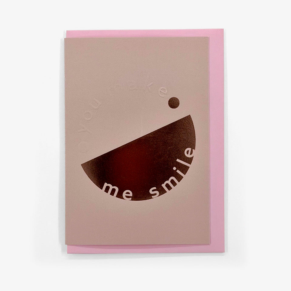 Pale lilac You Make Me Smile card with embossed lettering and pink foil graphic, shown with a pink envelope.