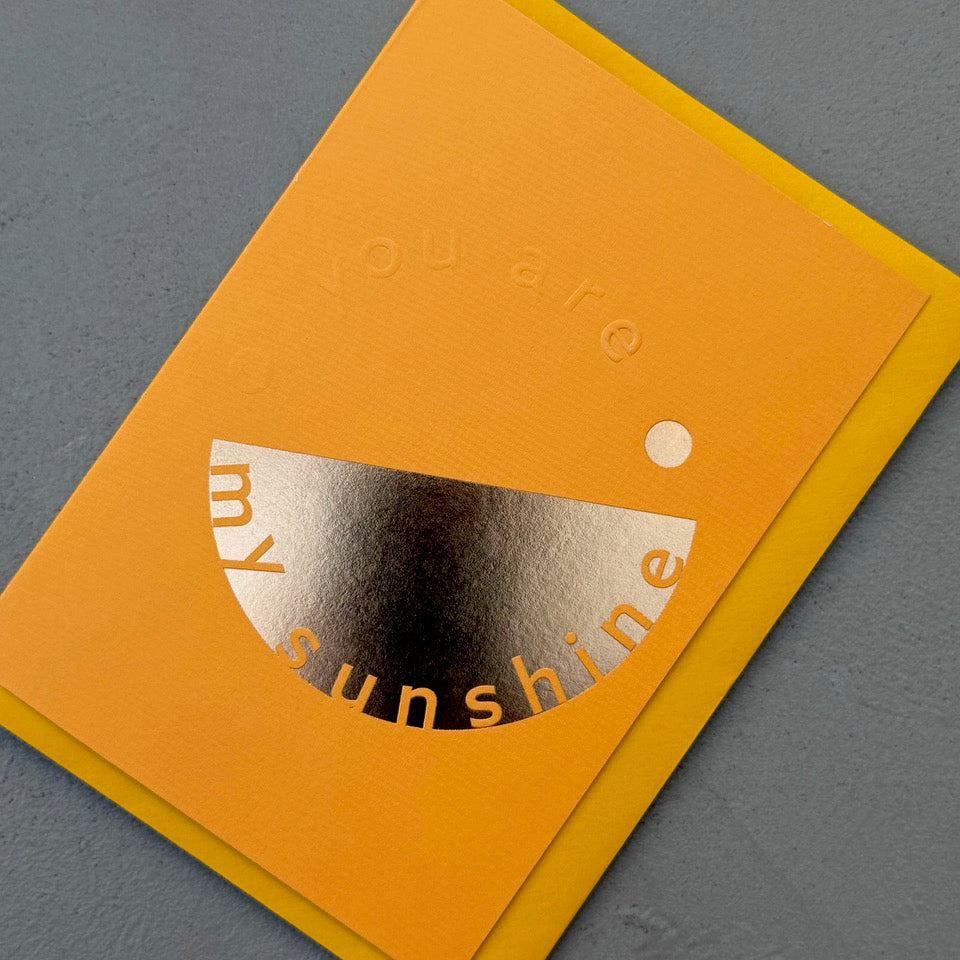 Angled view of the orange You’re My Sunshine card showing the embossed lettering and reflective gold foil.