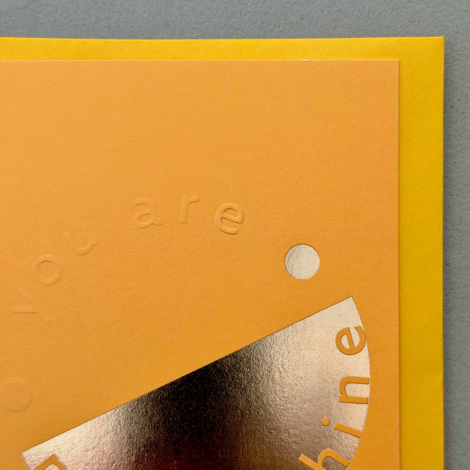Close-up of the embossed lettering and gold foil detail on the orange You’re My Sunshine card.
