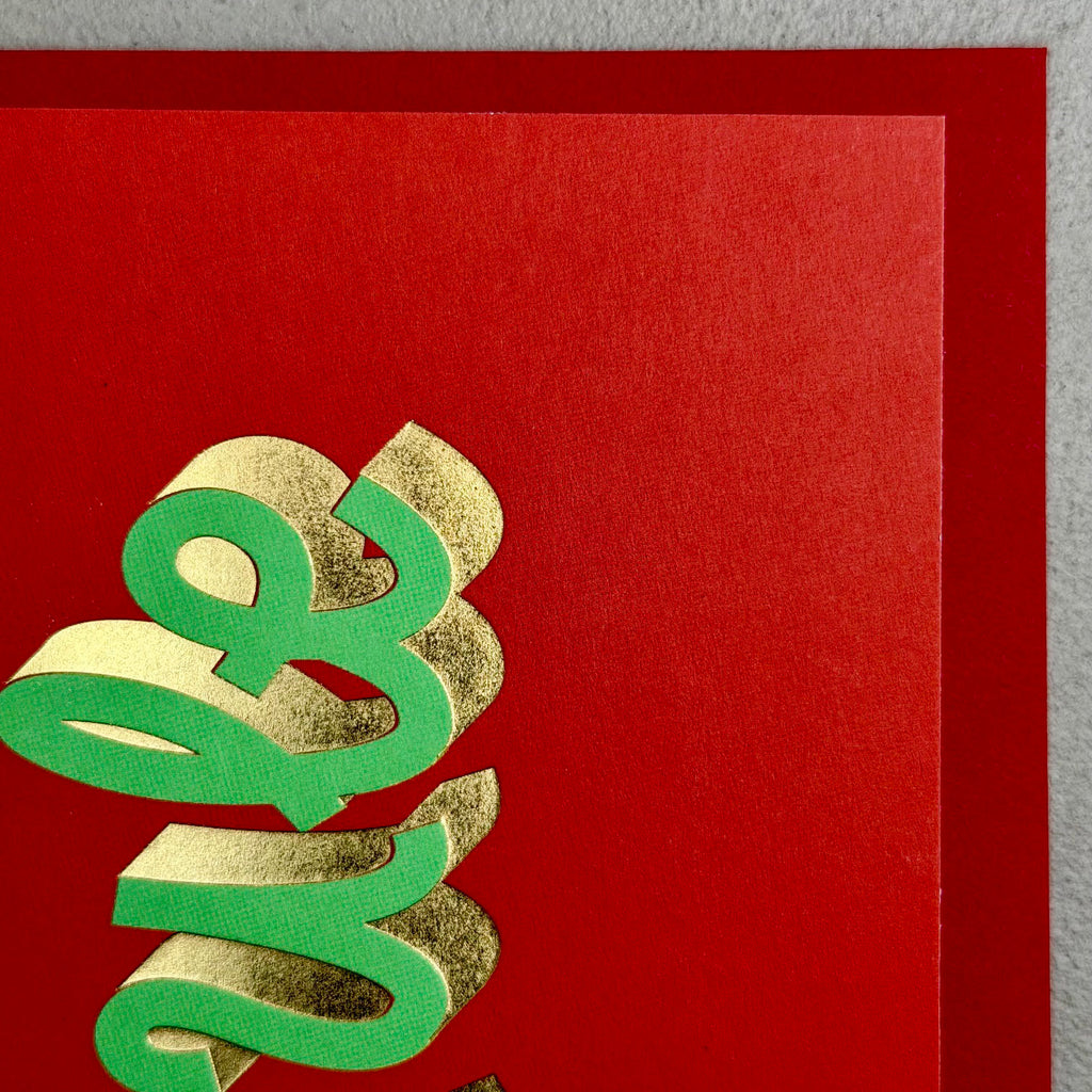 Close-up of YULE Christmas card showing sculptural green lettering and gold foil details
